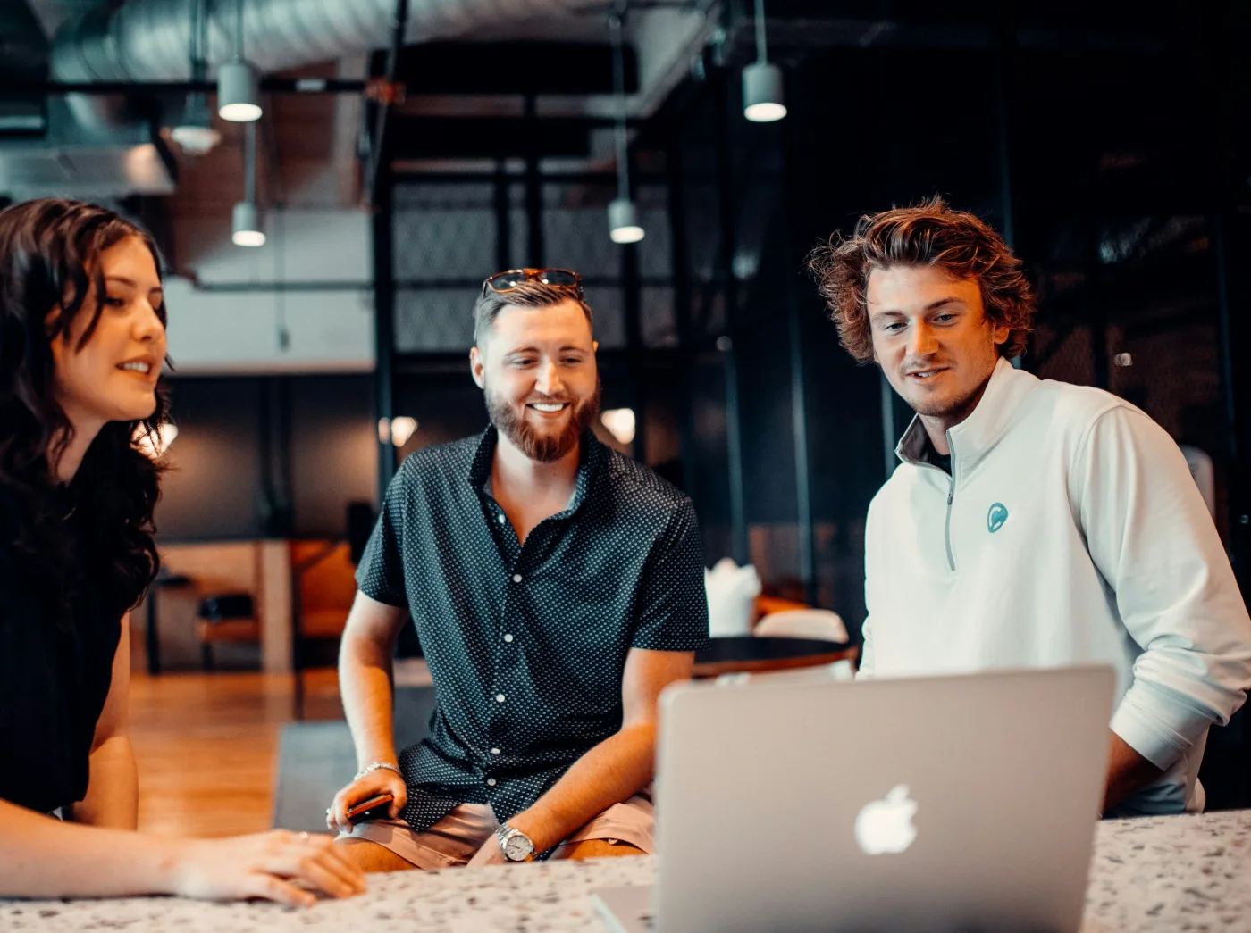 Three young professionals smile as they work together on a laptop